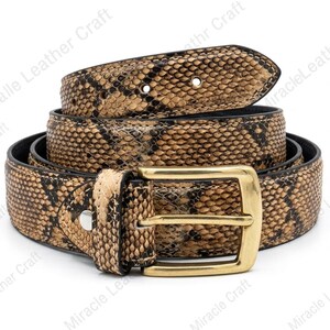 Könnte beinhalten: Ein brauner und schwarzer Gürtel mit Schlangenmuster und einer goldfarbenen rechteckigen Schnalle. Der Gürtel ist aufgerollt und zeigt die Textur und das Design. Der Gürtel ist aus Leder.