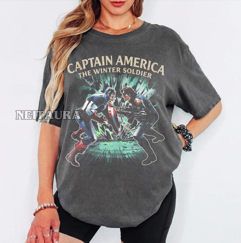 May include: Dark gray t-shirt featuring a graphic of Captain America and the Winter Soldier in a battle scene. The text "CAPTAIN AMERICA THE WINTER SOLDIER" is printed across the top in a vintage style.