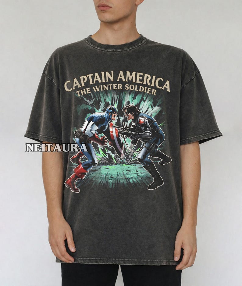 May include: Dark grey t-shirt with a graphic of Captain America and the Winter Soldier in combat. The text "CAPTAIN AMERICA THE WINTER SOLDIER" is printed above the image. The shirt has short sleeves and a crew neck.