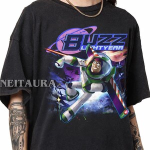 May include: Black t-shirt with a graphic of Buzz Lightyear in his spacesuit, with the words "Buzz Lightyear" in a retro font. The design includes a space scene with planets and stars.