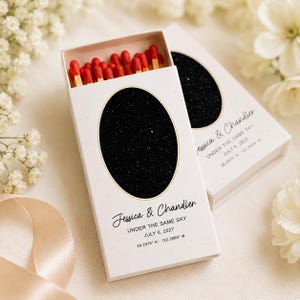 May include: Two white matchboxes filled with red-tipped matches. Each box features a black oval with a starry night sky design, gold trim, and the text Jessica & Chandler, UNDER THE SAME SKY, JULY 6, 2027, and 38.2975 N 122.2869 W.