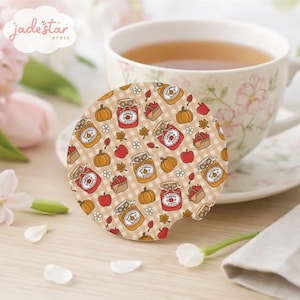 May include: A round car coaster featuring a beige and white gingham pattern decorated with illustrations of jars labeled pumpkin butter and apple jam, interspersed with small pumpkins, red apples, baskets of apples, and brown autumn leaves.