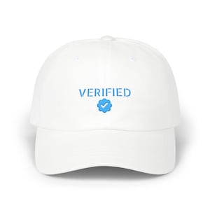 May include: A white baseball cap with the word "VERIFIED" in blue, along with a blue checkmark logo. The cap has a curved brim and a rounded crown. The hat is made of a soft material.
