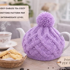 Puede incluir: Un calentador de té de punto lila con un diseño de punto de cable y un pompón en la parte superior. El calentador está sobre una tetera blanca. Una taza de té, un platillo y una cesta de galletas también están sobre la mesa. El texto en la imagen dice "Cosy Cables Tea Cozy Knitting Pattern PDF Intermediate Level".