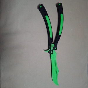 May include: A butterfly knife with a bright green blade and accents. The handles are black with green stripes. The knife is open, displaying the blade.