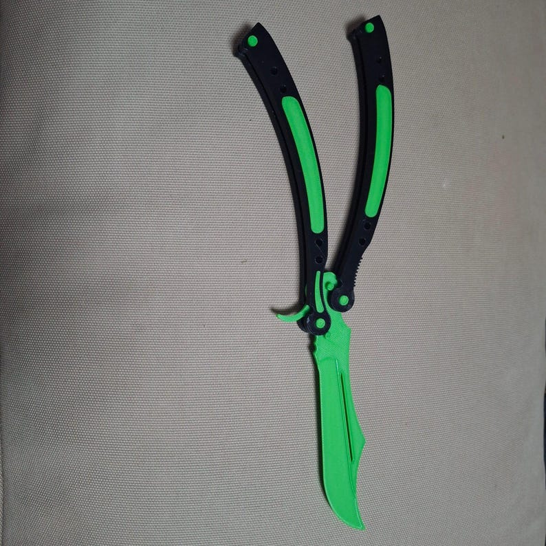 May include: A butterfly knife with a bright green blade and accents. The handles are black with green stripes. The knife is open, displaying the blade.