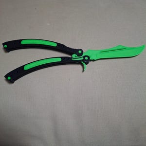 May include: A butterfly knife, featuring a vibrant green blade and accents. The handles are black with green inserts. The knife is open, showcasing the blade and handle design.
