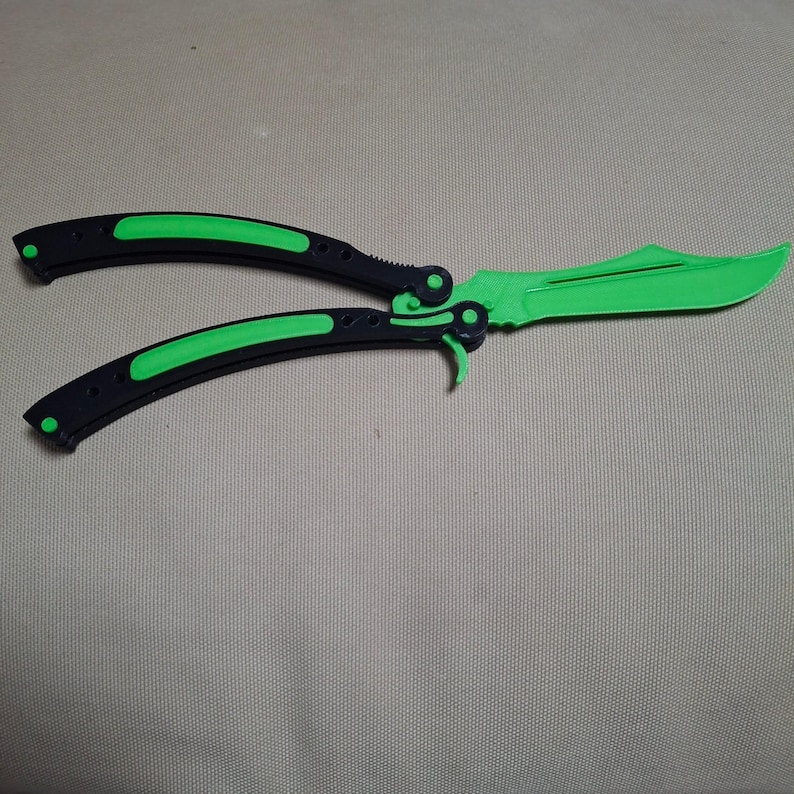 May include: A butterfly knife with a bright green blade and accents. The handles are black with green inserts. The knife is open, displaying the blade and the handle design.