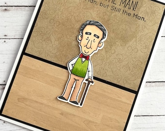 Könnte beinhalten: Eine Grußkarte mit einer Cartoon-Illustration eines älteren Mannes mit einem Stock. Die Karte hat einen braunen Hintergrund mit einem Muster und den Text "You're the Man! The Old Man, but Still the Man."