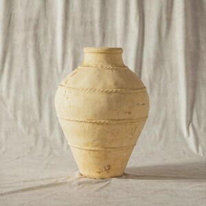 May include: An off-white vase with a textured finish and rope-style detailing. The vase has a rounded body and a narrower neck. The design features horizontal bands of rope-like texture. The neutral colour and simple design suggest a rustic aesthetic.