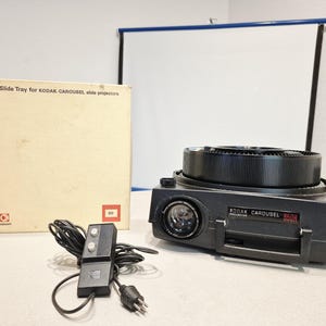 May include: A black Kodak Carousel 850H slide projector with a circular tray, a wired remote control with two buttons, and a beige cardboard box labeled Rotary Slide Tray for KODAK CAROUSEL slide projectors with a red square logo.