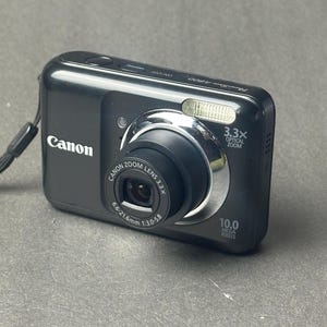 May include: A black Canon PowerShot A480 digital camera. The camera has a 3.3x optical zoom lens and 10.0 megapixels. The Canon logo is visible on the front of the camera.