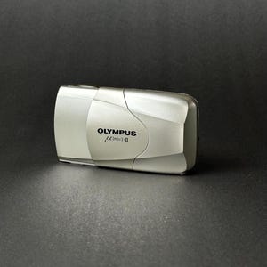 Op de afbeelding: Een witte keramische mok met een zwart handvat en de tekst "But First, Coffee" in een zwarte, handgeschreven lettertype. De mok staat op een wit oppervlak.