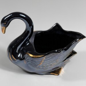 May include: A black ceramic swan-shaped planter with gold accents. The swan has a curved neck and a detailed wing design. The interior is hollow, suitable for small plants or decorative items.