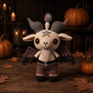 May include: A crocheted goat doll with large eyes, horns, and wings. The doll is wearing brown pants and has a pentagram on its chest. Pumpkins and autumn leaves are in the background, creating a Halloween theme.