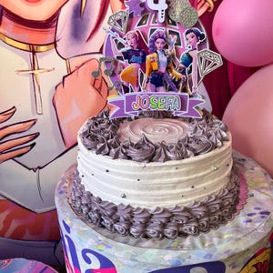 Puede incluir: Una tarta de cumpleaños de dos pisos con glaseado blanco y glaseado decorativo gris. La tarta está coronada con un adorno personalizado con personajes de dibujos animados, el número 4 y el nombre "Josefa". Globos rosas en el fondo.