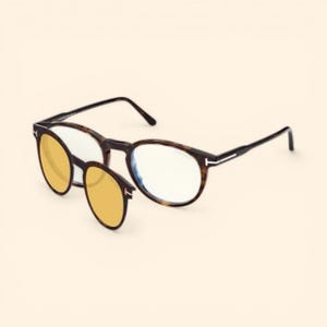 May include: Brown tortoiseshell eyeglasses with a clip-on yellow-tinted lens. The glasses have a round frame and black temples. The clip-on lens is also round and attaches to the main frame.