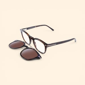 Peut inclure: Une paire de lunettes à monture écaille de tortue avec un clip solaire. Les lunettes ont des verres transparents, tandis que le clip solaire a des verres bruns. L'ensemble est présenté sur un fond neutre.