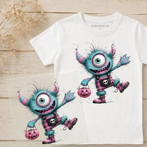 Könnte beinhalten: Ein weißes Kurzarm-T-Shirt mit einer Grafik eines flauschigen, türkisfarbenen einäugigen Monsters in einer rosa karierten Latzhose mit Totenkopf-Emblem, das einen rosa Kürbis hält. Der Text KLEINER ENTDECKER - BIO steht im inneren Halsausschnitt.