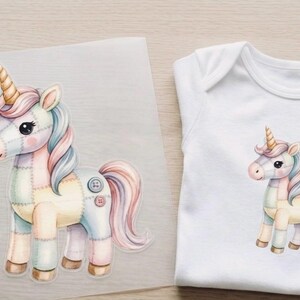 Könnte beinhalten: Aquarell-Illustration eines pastellfarbenen Einhorns mit goldenem Horn, Knopfdarstellungen und fließender Mähne und Schweif. Das Bild befindet sich auf einer transparenten Folie und ist auch auf einem weißen Baby-Body abgebildet.