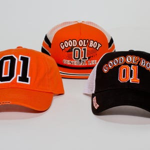 May include: Three baseball caps in orange and black. The orange caps have the number "01" in white. The black cap has a white mesh back and the words "GOOD OL' BOY 01" in orange.