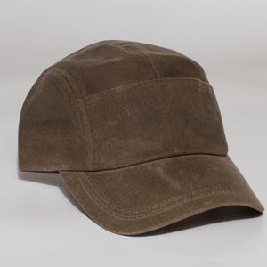Puede incluir: Gorra marrón de cinco paneles con visera corta. La gorra tiene un diseño estructurado con un panel rectangular en la parte delantera y una visera curva. El sombrero está hecho de un material texturizado y duradero.