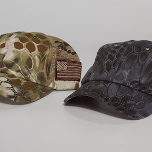 May include: Two baseball caps with a camouflage pattern. One cap is in shades of brown and green, the other in gray and black. Both have a small American flag patch on the side.