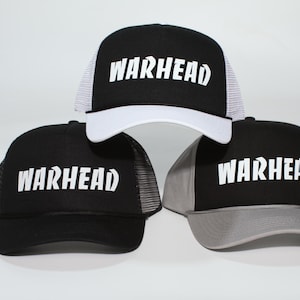 May include: Three black trucker hats with the word "WARHEAD" in white block letters. Each hat has a different colored mesh backing: white, black, and gray. The hats are displayed against a white background.