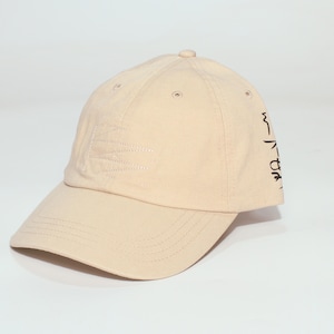 Puede incluir: Gorra de béisbol beige con visera curva. La gorra tiene un diseño cosido en la parte delantera y texto negro en el lateral. Tiene un botón en la parte superior y pequeños orificios de ventilación.