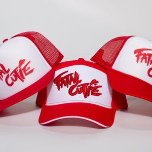 May include: Three trucker caps featuring a white front panel and red mesh back. Each cap displays the text "FATAL CUTIE" in bold red lettering across the front. The caps have a red brim and a structured design with a snapback closure visible on the back.