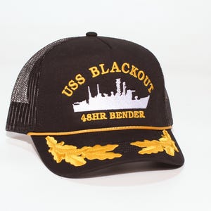 May include: Black trucker hat with a mesh back and a curved brim. The front features the text "USS BLACKOUT" above a white ship illustration and "48HR BENDER" in gold. Gold leaf embroidery accents the brim.