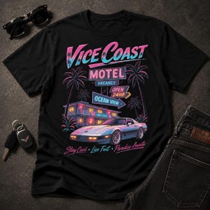 May include: A black t-shirt featuring a graphic print of a retro motel and a sports car. The text reads Vice Coast, Motel, Vacancy, Open 24HR, Ocean View, and Stay Cool, Live Fast, Paradise Awaits. The design uses neon pink and blue color accents.