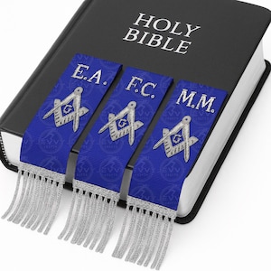 May include: A black Holy Bible with three blue ribbon bookmarks. Each bookmark has silver fringe and a silver emblem with the letters E.A., F.C., and M.M. The Bible's cover has the words "HOLY BIBLE" in white.
