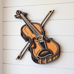 Puede incluir: Una pieza de arte mural de violín de madera en capas. El violín es de color naranja cálido con detalles en negro y gris. El arco está colocado sobre el violín. La obra de arte está montada sobre un fondo blanco con listones horizontales.