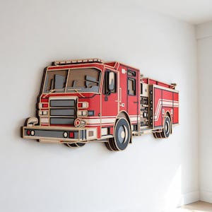 May include: A wooden wall art piece showing a red fire engine with white and grey details. The fire engine has detailed cutouts of windows, lights, and wheels. The artwork is mounted on a white wall, highlighting the layered design.