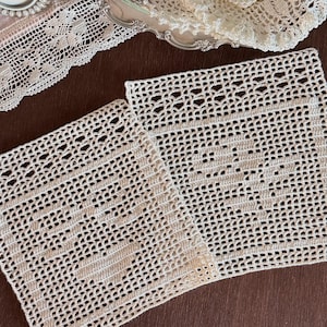 May include: Two square off-white crochet doilies featuring an intricate openwork grid pattern with a solid central motif. The handmade lace pieces display a delicate texture and are crafted with fine thread, showcasing a repeating geometric design.