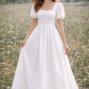 May include: A white linen dress with a square neckline and short, puffed sleeves. The dress has a fitted bodice and a flowing skirt. The woman is standing in a field of wildflowers.
