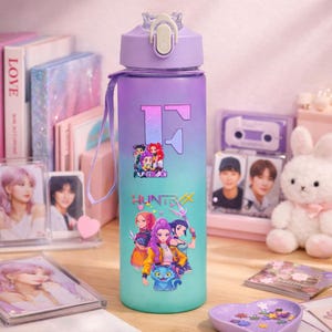 Könnte beinhalten: Eine lilafarbene und türkisfarbene Wasserflasche mit weißem Deckel und passendem Trageriemen. Die Flasche hat einen großen Buchstaben "F" und eine Cartoon-Grafik mit dem Wort "HUNTRAX". Die Flasche ist von anderen dekorativen Gegenständen umgeben.