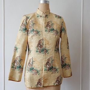 Könnte beinhalten: Eine Vintage-Jacke mit langen Ärmeln und Stehkragen. Die Jacke ist hellgelb und hat ein sich wiederholendes Muster von Tigern in einer naturalistischen Umgebung. Die Kanten sind mit goldfarbenem Material verziert.