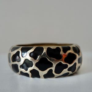 May include: A black and white patterned ring with a silver band. The pattern resembles a giraffe print.