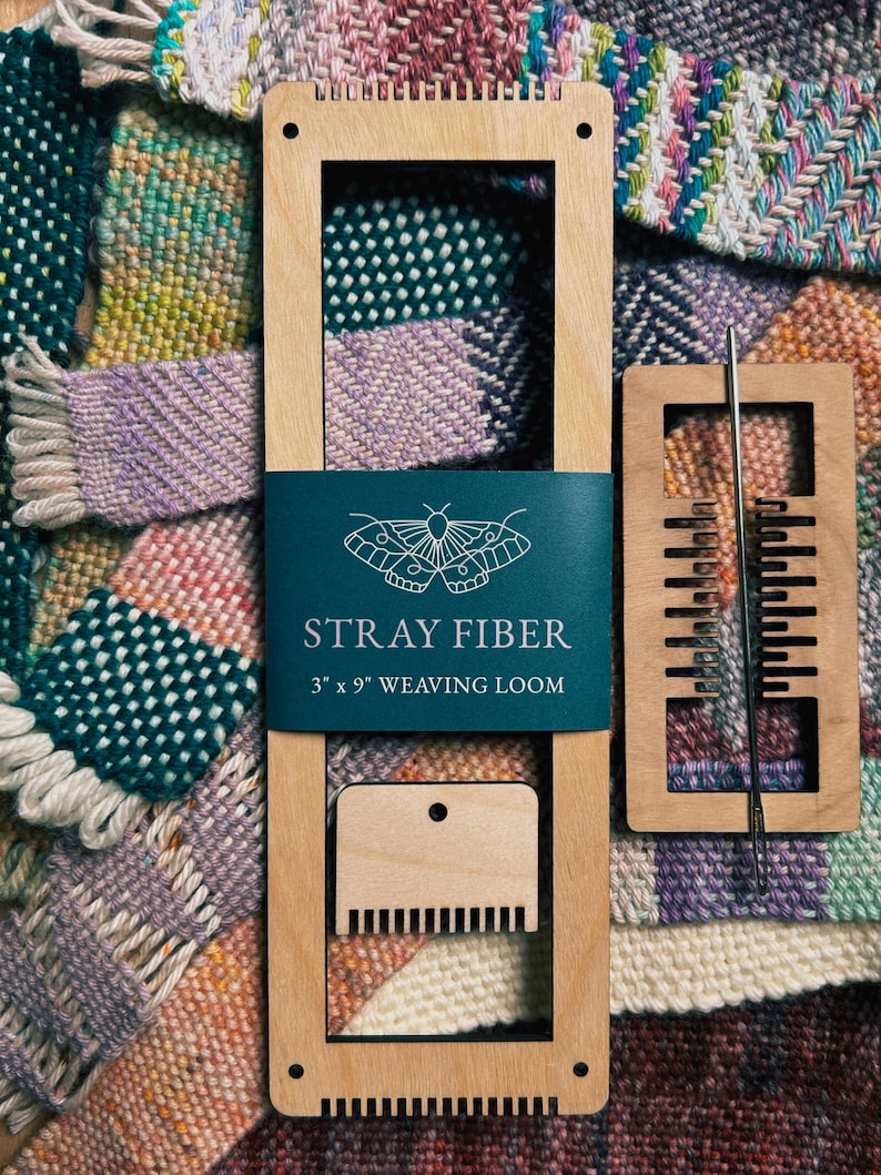 Może przedstawiać: Drewniane krosno tkackie z turkusową etykietą z napisem "STRAY FIBER 3" x 9" WEAVING LOOM". Dołączona jest igła tkacka i grzebień. Tło przedstawia kolorowe pr&oacute;bki tkanin tkanych.