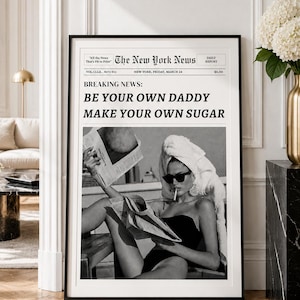 May include: A framed black and white wall art print styled as a newspaper titled The New York News. The headline reads BREAKING NEWS: BE YOUR OWN DADDY MAKE YOUR OWN SUGAR. It features a person in a towel and sunglasses reading a newspaper.