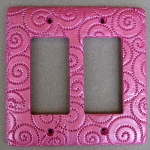 May include: A pink double light switch cover with a swirl pattern.