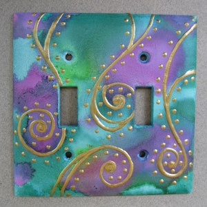 May include: A decorative light switch cover with a teal, purple, and gold abstract design. The design features swirls and dots.