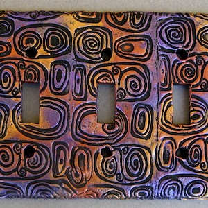 May include: A triple light switch cover with a decorative design of swirling black lines on a purple and orange background.