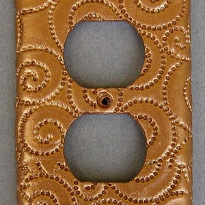 May include: A gold-colored outlet cover with a decorative pattern of swirls and dots.