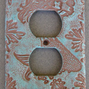 May include: A decorative outlet cover with a turquoise and brown design. The cover features a stylized floral pattern with a textured surface.