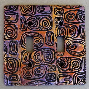 May include: A double light switch cover with a decorative design of swirling black lines on a purple and orange background.