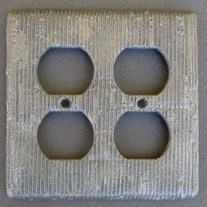 May include: A silver metal outlet cover with a textured surface and four cutouts for electrical outlets.