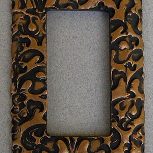 May include: A decorative light switch cover with a black and copper floral design.